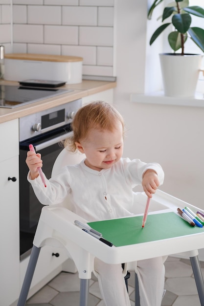 フェルトペンを使用して絵を描くハイチェアに座っている左利きの子供幼児
