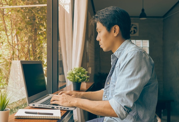 Left view young asian casual businessman using laptop in coffee shop in vintage tone