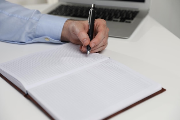 Lefthanded man writing in notebook at white table closeup