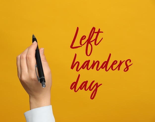 Lefthanded woman holding pen on yellow background closeup