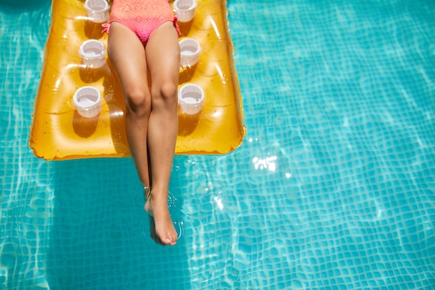 Leg of little girl in swimming pool, swims on inflatable yellow mattress, family vacation, tropical holiday resort, view from above, copy space.