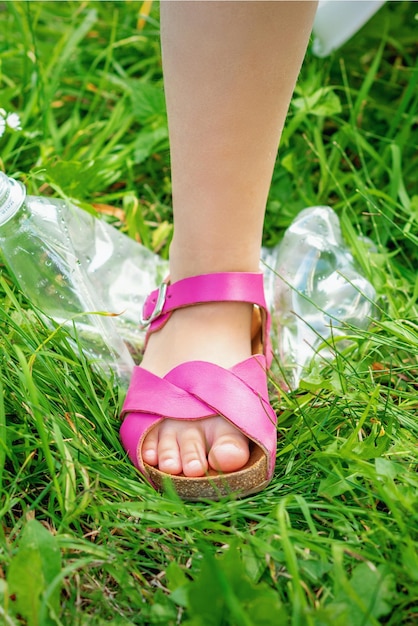 La gamba di una bambina calpesta una bottiglia di plastica sull'erba verde del parco