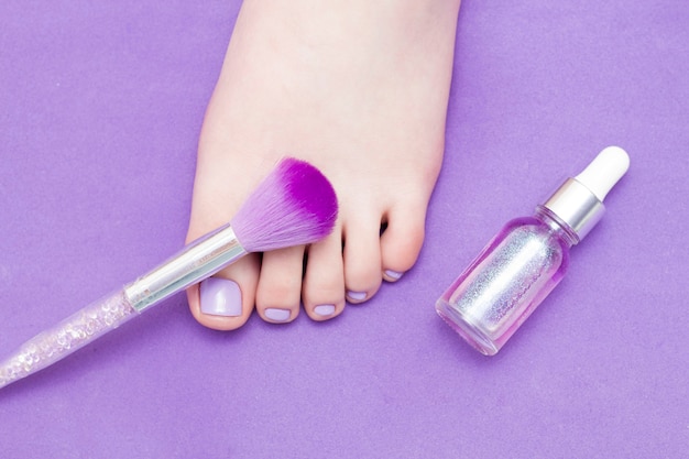 A leg on a purple background, next to a fluffy nail brush.\
pedicure. purple tone