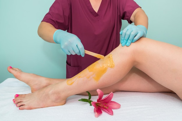 Leg sugaring A beautician makes a sugar paste depilation of a woman's legs in a beauty salon Female aesthetic cosmetology Apply sugar paste with a wooden spatula