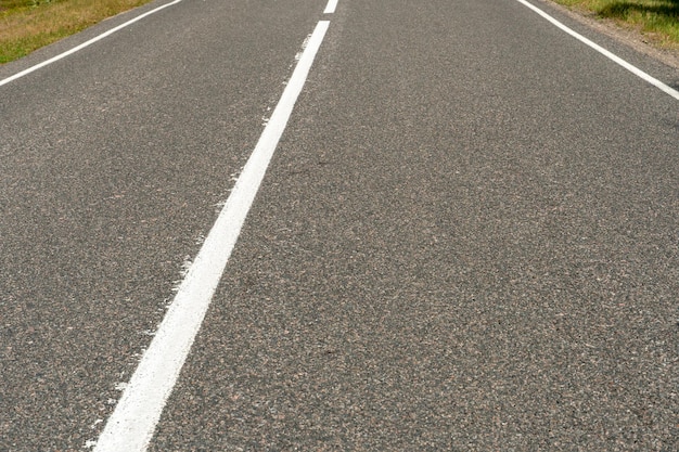 Lege asfaltweg door bossen en velden Nieuwe verse asfaltverharding weg van de stad Ontwikkeling van landelijke infrastructuur Wegmarkeringslijnen close-up