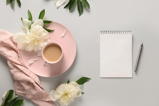 Lege blanco voor planning met koffiekopje witte pioenrozen op grijs bureau