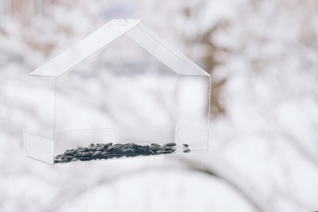 Lege doorzichtige vogelvoeder met zaden op het raam tegen een achtergrond van sneeuw close-up.