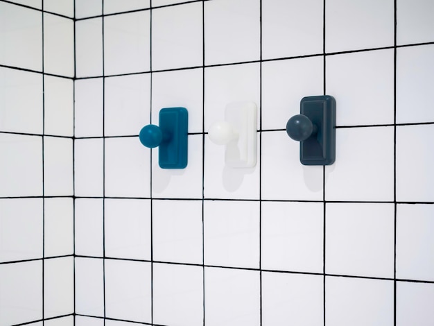 Lege drie moderne handdoekhaken, blauw en wit, hangend aan een witte achtergrond in de badkamer van de rastermuur met een minimalistische stijl van kopieerruimte