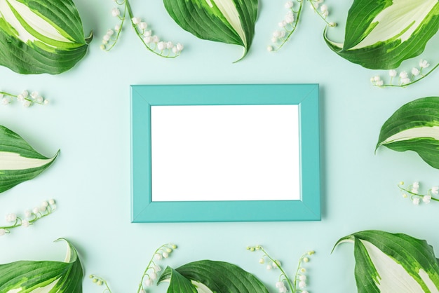 Lege fotolijst in frame gemaakt van lente lelietje-van-dalen bloemen op pastelblauw oppervlak