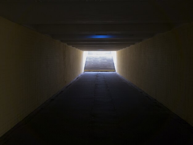 Foto lege gele ondergrondse voetgangersoversteekplaats. tunnel en daglicht aan het einde. trap naar boven bij het zebrapad. een lange betonnen tunnel met lantaarns in de stad ondergronds.