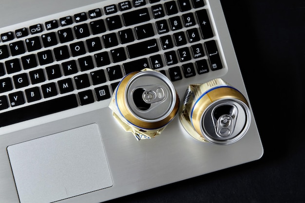 Lege geplette blikjes bier op een laptoptoetsenbord op een zwarte achtergrond Dronken conflicten in sociale netwerken