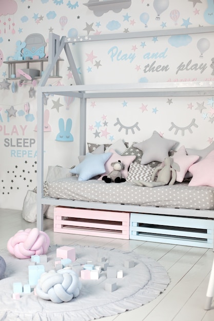 Foto lege gezellige kinderkamer met een witte muur met stickers, speelgoed, een bed met kussens. scandinavische interieur van een kinderkamer. houten bed in de vorm van huis met speelgoed en een deken. kleuterschool