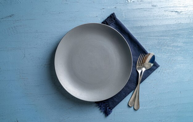 lege grijze plaatvork en lepel op lichtblauwe houten tafel met donkerblauw tafelkleed Bovenaanzicht Mock up