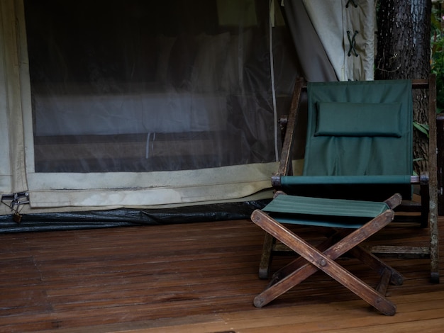 Lege houten campingstoel met groene stoffen zitting en voetsteun op het terras voor de kamer van grote tent Opvouwbare buitenzonnebank op witte glamping-tent