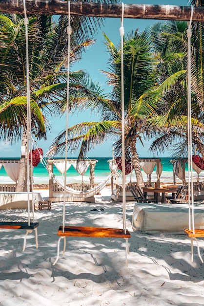 Lege houten schommelstoelen die aan een houten frame op zand hangen in een prachtig strandresort met luifel en hangmat in Tulum, Mexico