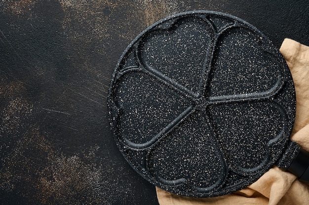 Lege koekenpan zwart, koekenpan met stenen antiaanbaklaag voor het bakken van pannenkoeken in de vorm van ontbijtharten en ingrediënten op grijze betonnen tafelondergrond. Ontbijt voor Valentijnsdag. Bovenaanzicht.