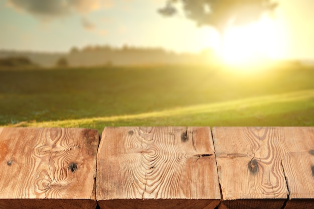 Lege leeftijd getextureerde harde houten tafel op een wazig natutal landelijke zonsondergang landschap-achtergrond voor bloot en montage van uw producten.