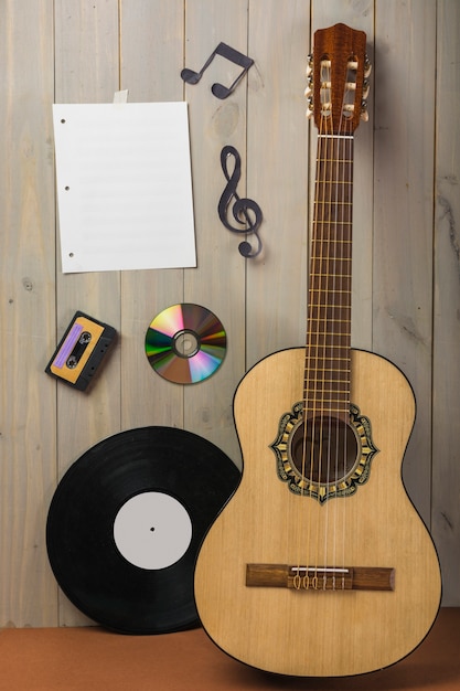 Lege muzikale pagina; cassette; compact disc; en muzieknoot vast op houten muur met gitaar en vinyl record