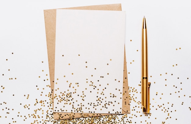 Lege nota met envelop, pen en gouden glittersterren op witte achtergrond