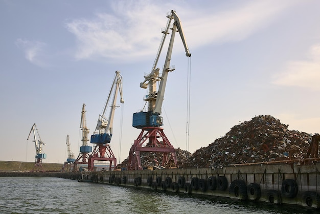 Lege pier in haven met torenkranen en grote hoop schroot