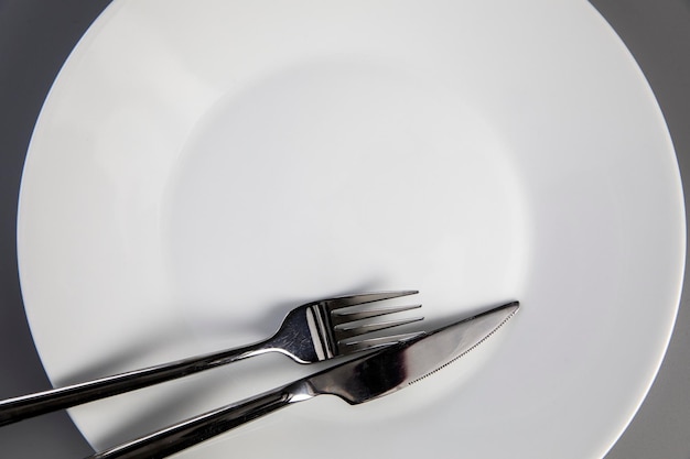 Lege plaat met vork en mes op grijze bovenaanzicht als achtergrond voor kopieerruimtevoedsel en gezond eten