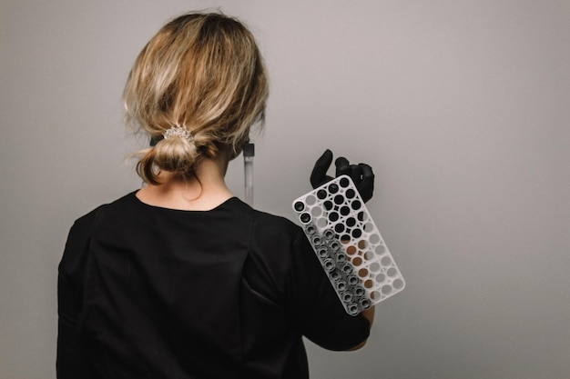 Lege reageerbuis in een glazen kolf in de handen van een wetenschapper of schoonheidsspecialist Zwarte handschoenen op een grijze achtergrond Experiment analyseert meisje van achteren