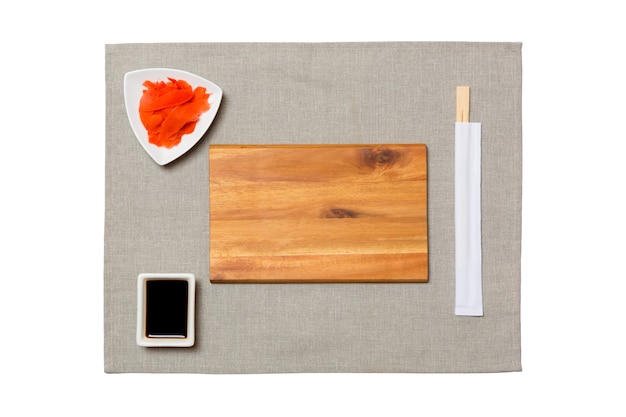 Lege rechthoekige bruine houten plaat met stokjes voor sushi, gember en sojasaus op grijze servetachtergrond. Bovenaanzicht met kopie ruimte voor u ontwerpen.