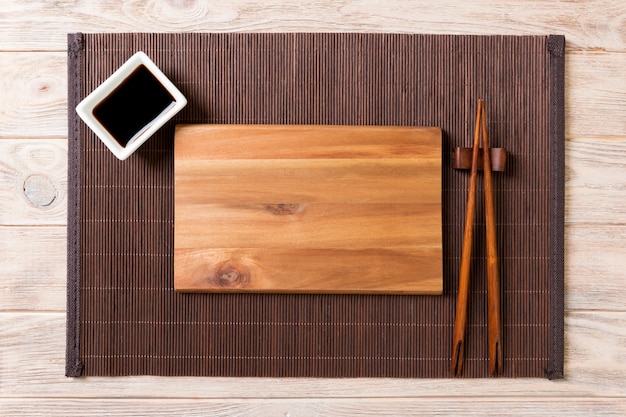 Lege rechthoekige houten plaat voor sushi met saus en eetstokjes op houten tafel, bovenaanzicht
