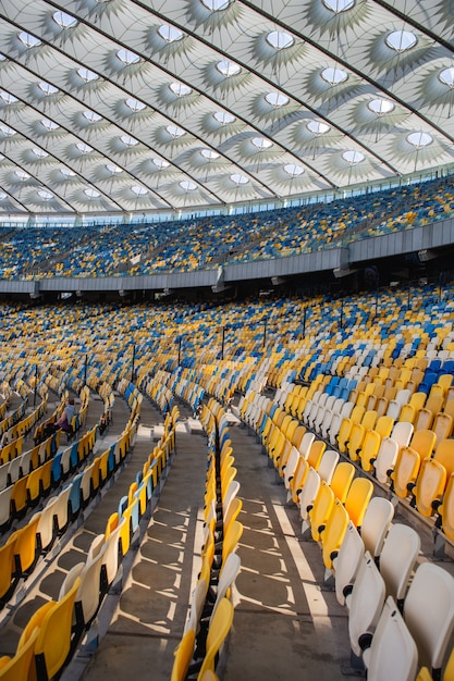 Lege rijen stoelen in een olympisch voetbalstadion met gele en blauwe banken