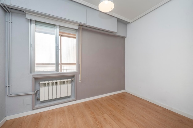 Lege ruimte met eiken houten vloer grijze muren en aluminium radiator met een raam dat communiceert met een gesloten terras