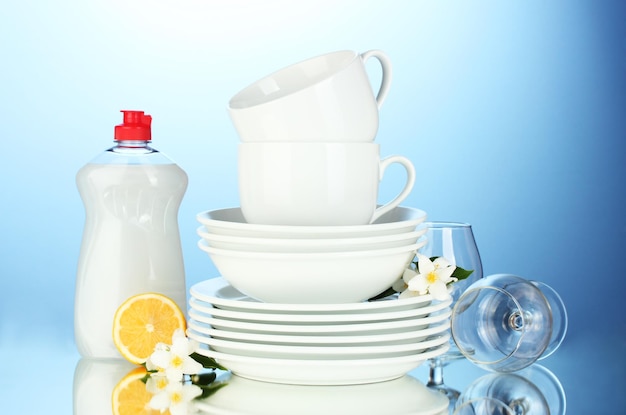 lege schone borden glazen en bekers met afwasvloeistof en citroen op blauwe achtergrond