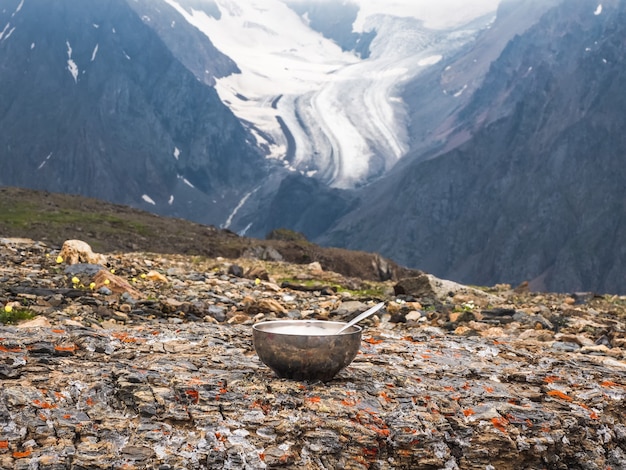 Lege toeristenkom met een lepel is aangelegd op een steen tegen de achtergrond van een gletsjer en hoge bergen. lunchtijd, trekking op grote hoogte.