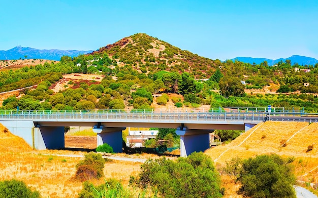 Lege weg zonder auto's onder de brug bij Villasimius op het eiland Sardinië in de zomer van Italië. Vervoer rijden op de snelweg van Europa. Vakantie op snelweg. provincie Cagliari. Bergen. Gemengde media.