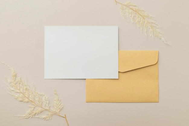 Lege wenskaartuitnodiging Mockup 5x7 op bruine envelop met gedroogde bloemen op beige achtergrond plat lag mockup