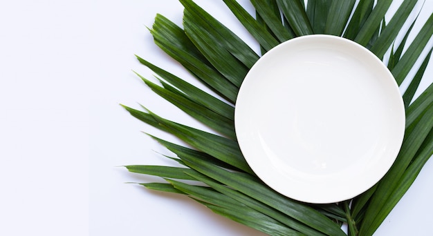 Lege witte ceramische plaat op tropische palmbladen op witte achtergrond. Bovenaanzicht
