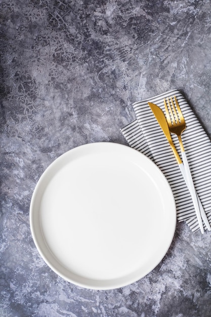 Lege witte plaat met servet voor voedselrecept en menurestaurant op stenen tafel en donkere achtergrond. Bovenaanzicht. Plat ontwerp.