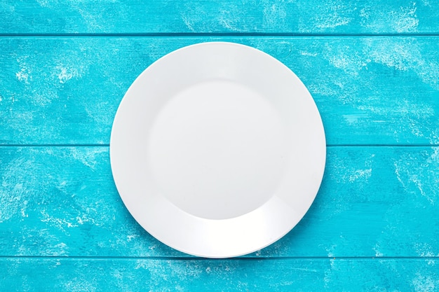 Lege witte ronde plaat op blauwe houten tafel. Bovenaanzicht. Mockup voor voedselproject.