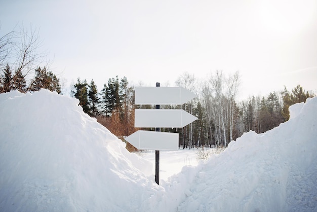 Lege witte wijzers, wegwijzer tegen de achtergrond van de de winteraard. richtingpijltekens op paal in besneeuwd bos. kerstmis en nieuwjaar concept.