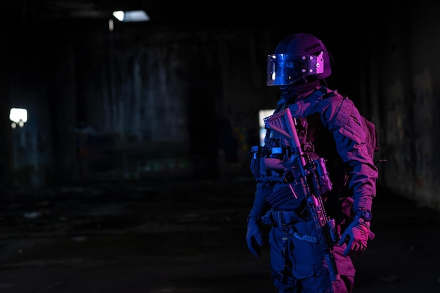 Legersoldaat in gevechtsuniformen met een aanvalsgeweer en gevechtshelm nachtmissie donkere achtergrond. Blauw en paars gellichteffect. Foto van hoge kwaliteit