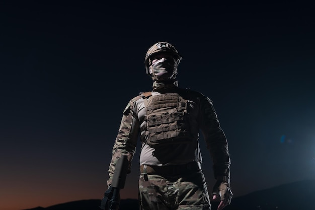 Legersoldaat in gevechtsuniformen met een aanvalsgeweer, plaatdrager en gevechtshelm op een gevaarlijke missie op een regenachtige nacht. Foto van hoge kwaliteit