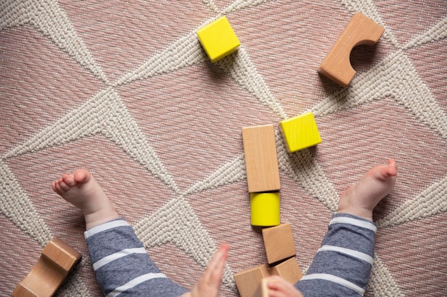 Legs of a baby spread out on a rug surrounded with wooden play blocks