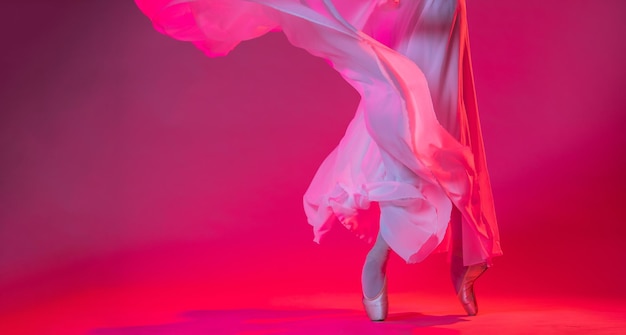 Legs of a ballerina in pointe shoes stand on a pink background