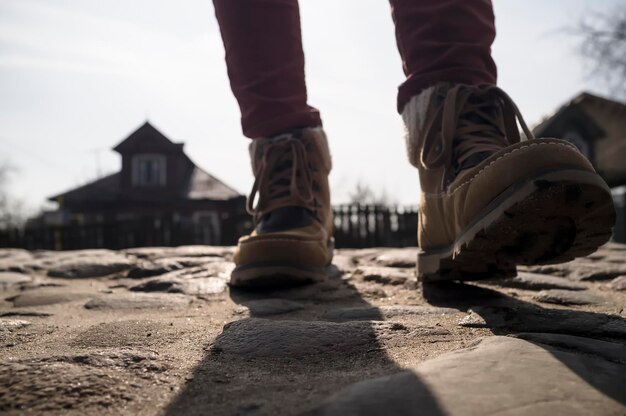 ブーツの脚は、背景の木造家屋で、石の古い石畳の舗装に沿って散歩します。