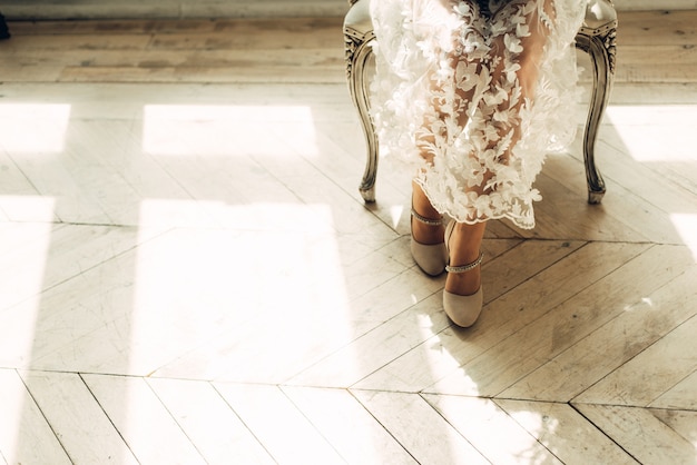Photo legs of the bride sitting on a chair, sunlight and a bright studio with free space