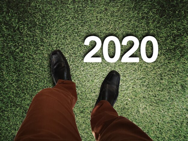 Legs of business man standing on grass floor with 2020