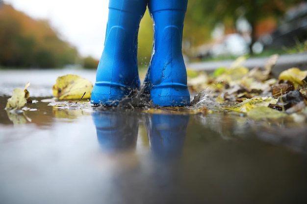 Gambe del bambino con stivali di gomma blu che saltano nelle pozzanghere autunnali