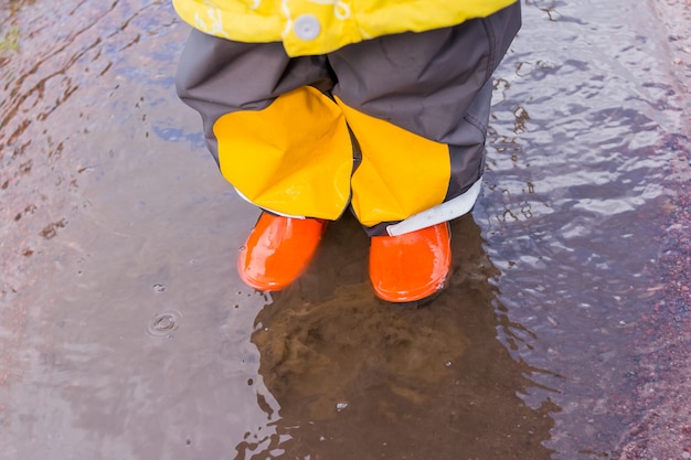 legs of child in orange rubber boots jumping in the autumn puddles. kids bright rubber boots