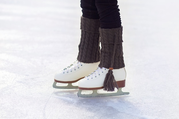 Le gambe dei pattini sono sul ghiaccio sulla pista. primo piano bianco classico dei pattini di figura. scaldamuscoli caldi lavorati a maglia con nappe