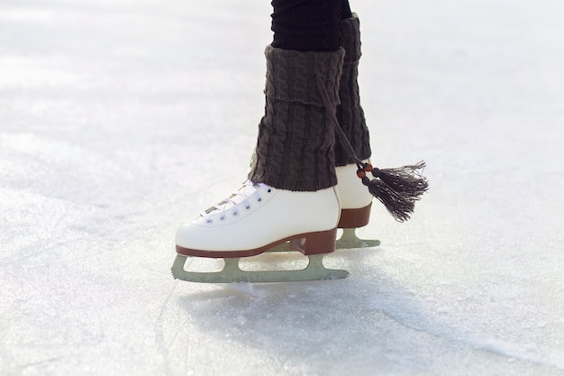 Legs in figure skates are on the ice on the rink. Classic white figure skates close-up. Knitted warm leg warmers with tassels