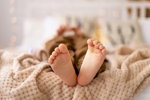 ベージュブラウンの自然な色調のベッドの上の小さな子供の焦点の足の足